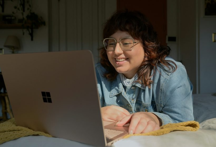 Mujer joven con lentes sonriendo frente a su computadora portátil durante una evaluación en línea desde su casa