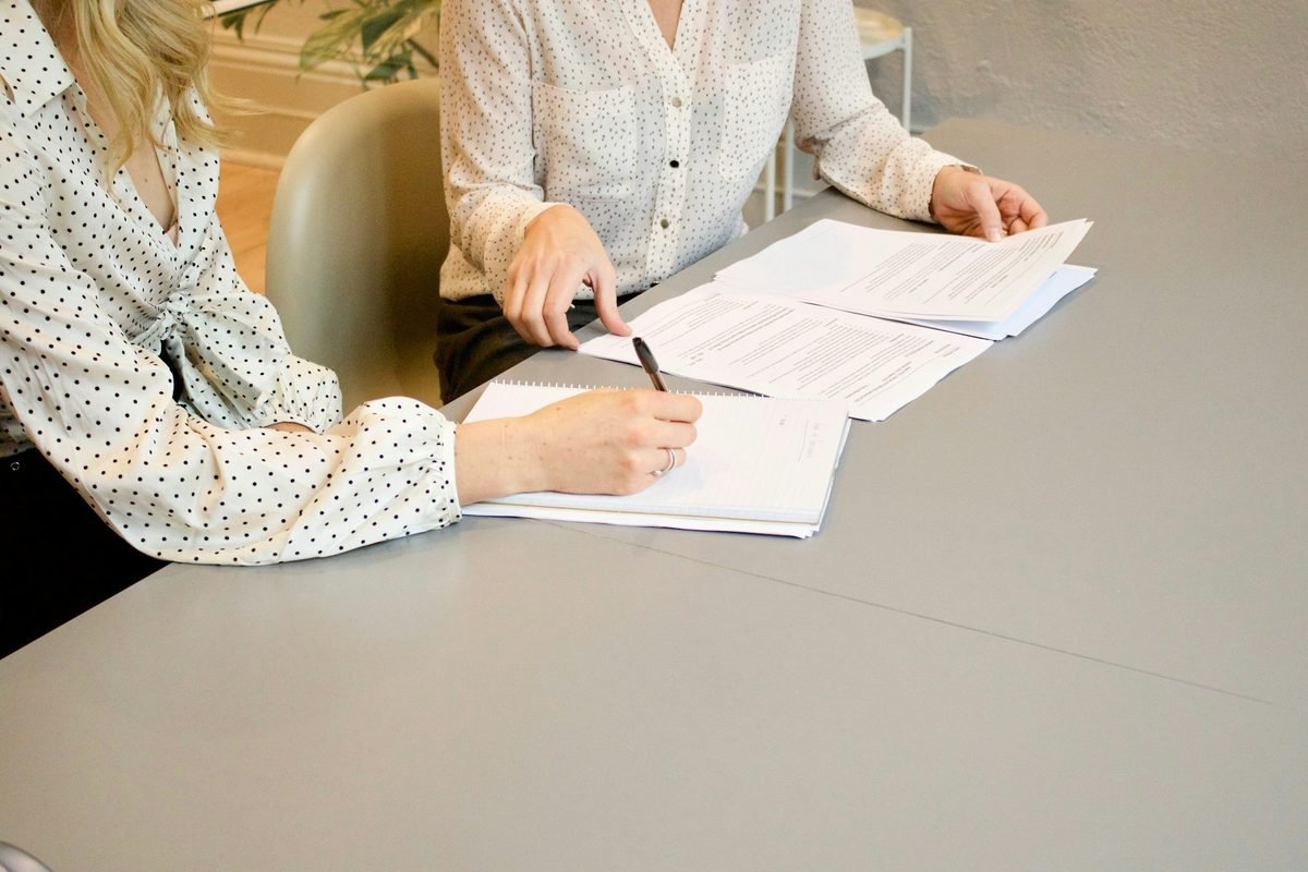 Dos personas firman documentos de vivienda en una mesa, como al presentar una carta de apoyo emocional al arrendador