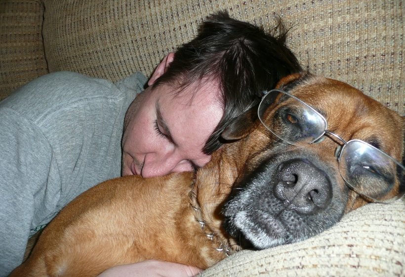 Hombre descansando con la cabeza apoyada sobre su perro grande en el sofá de su casa