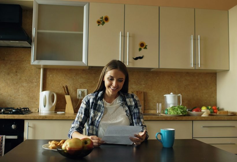 Inquilina sonriente leyendo su carta de apoyo emocional sentada a la mesa de la cocina