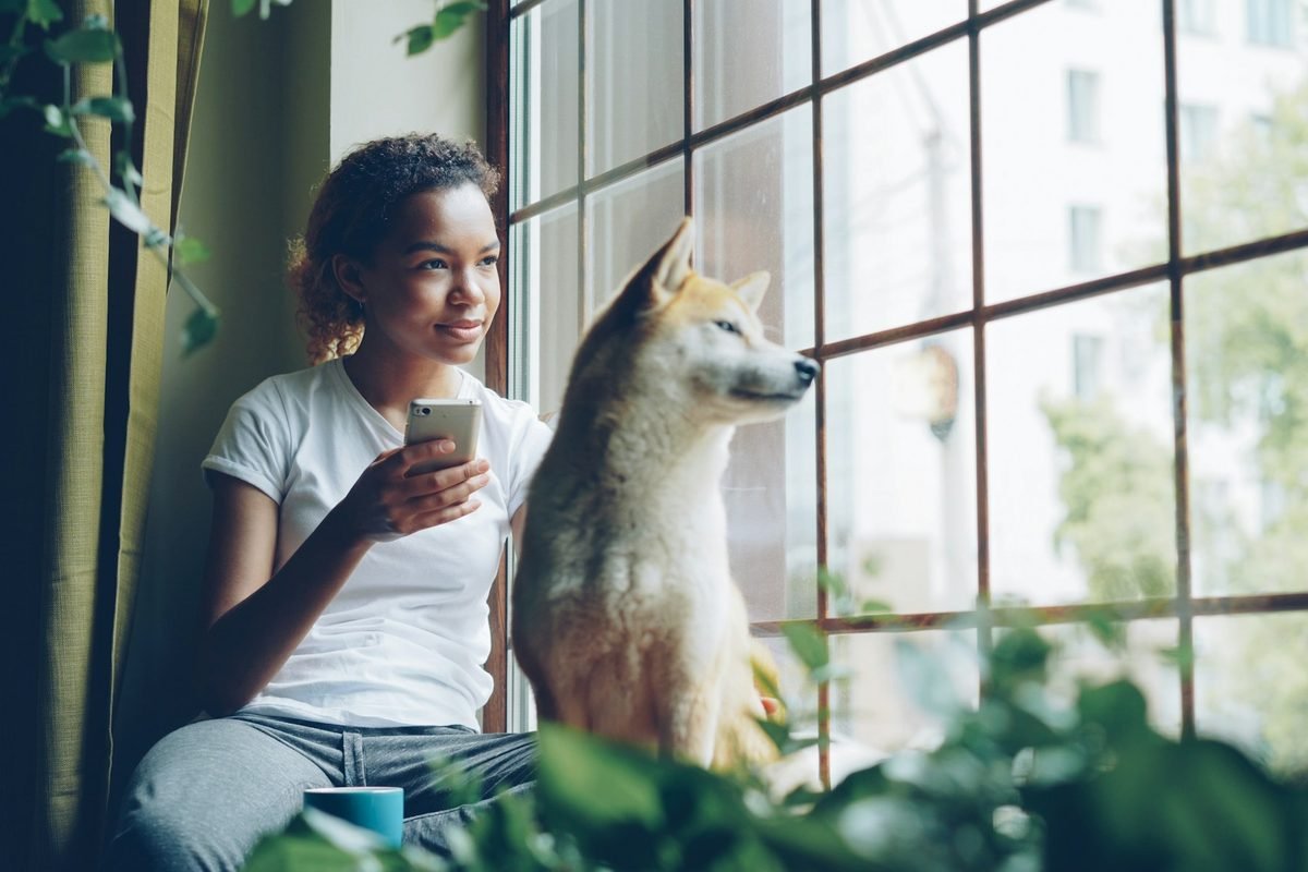 Mujer y su perro de apoyo emocional mirando juntos por la ventana de su apartamento